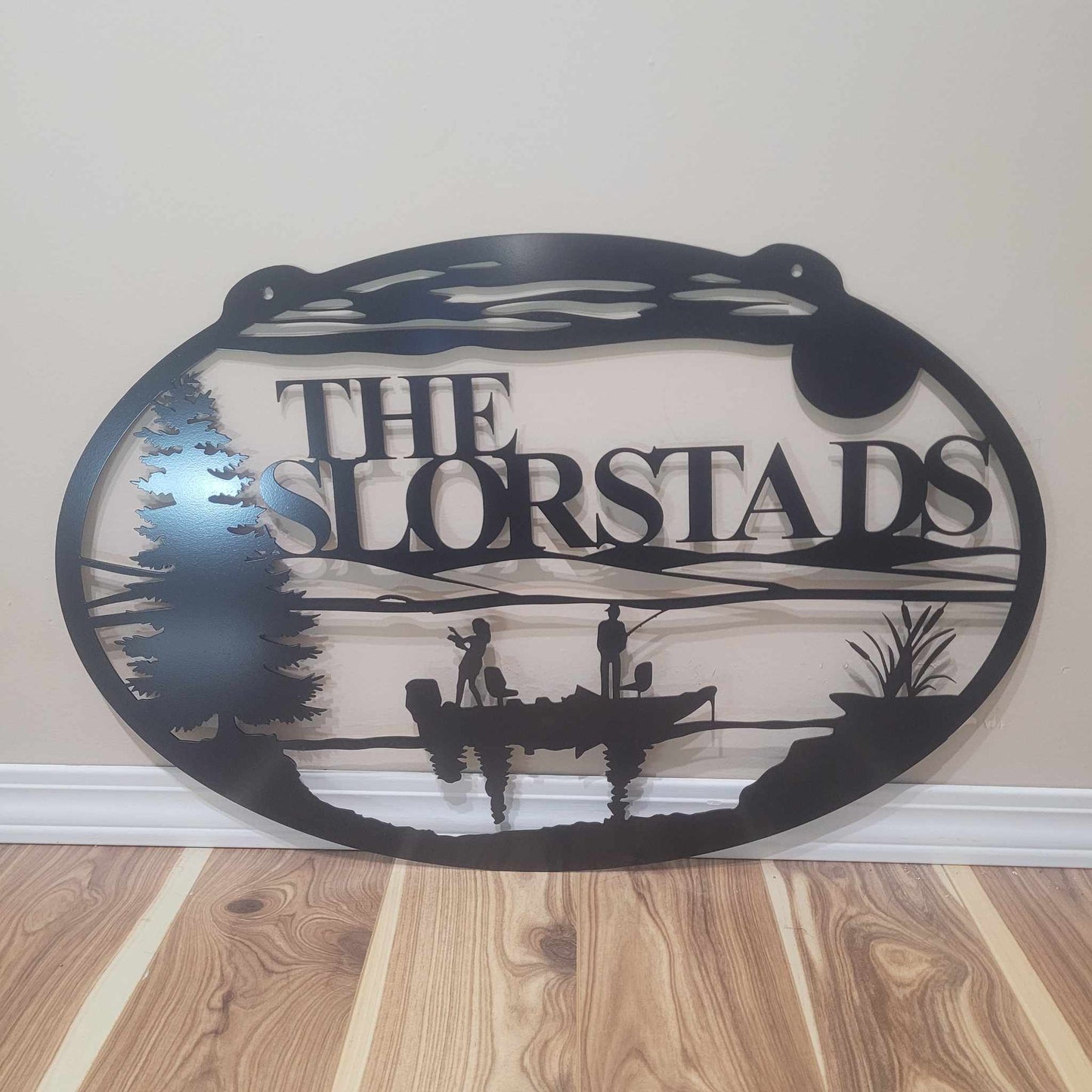 Decorative metal sign with 'The Slorstads' text and fishing design on a wooden floor.
