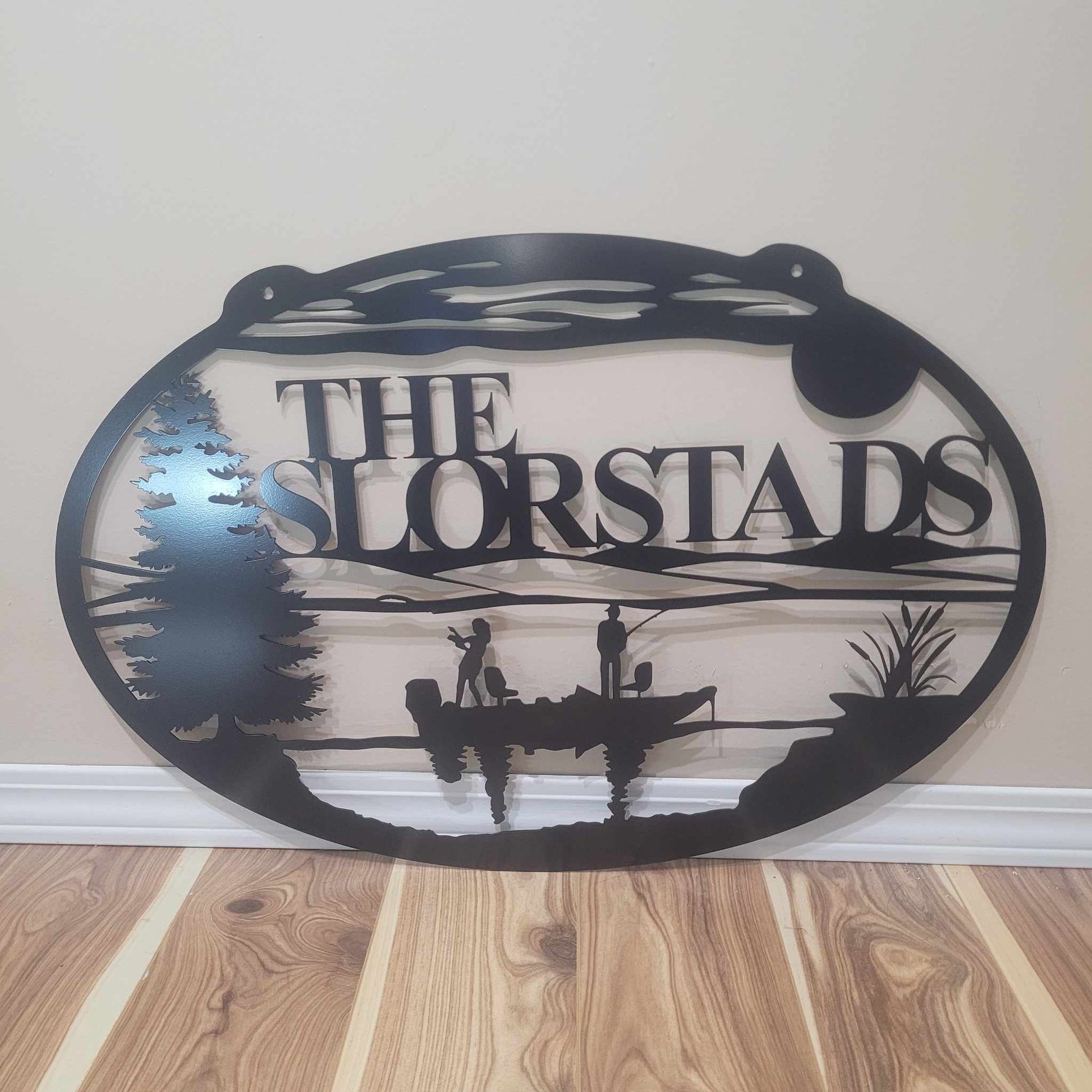 Decorative metal sign with 'The Slorstads' text and fishing design on a wooden floor.